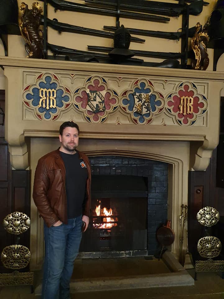 me-by-fire john wilson web design aigburth. A picture of John stood in front of a grand fireplace