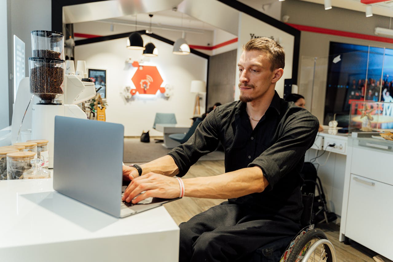 a man in a wheelchair using a laptop. Possibly looking at an article about how to use AI to improve readability of content for ALL users on John Wilson Design