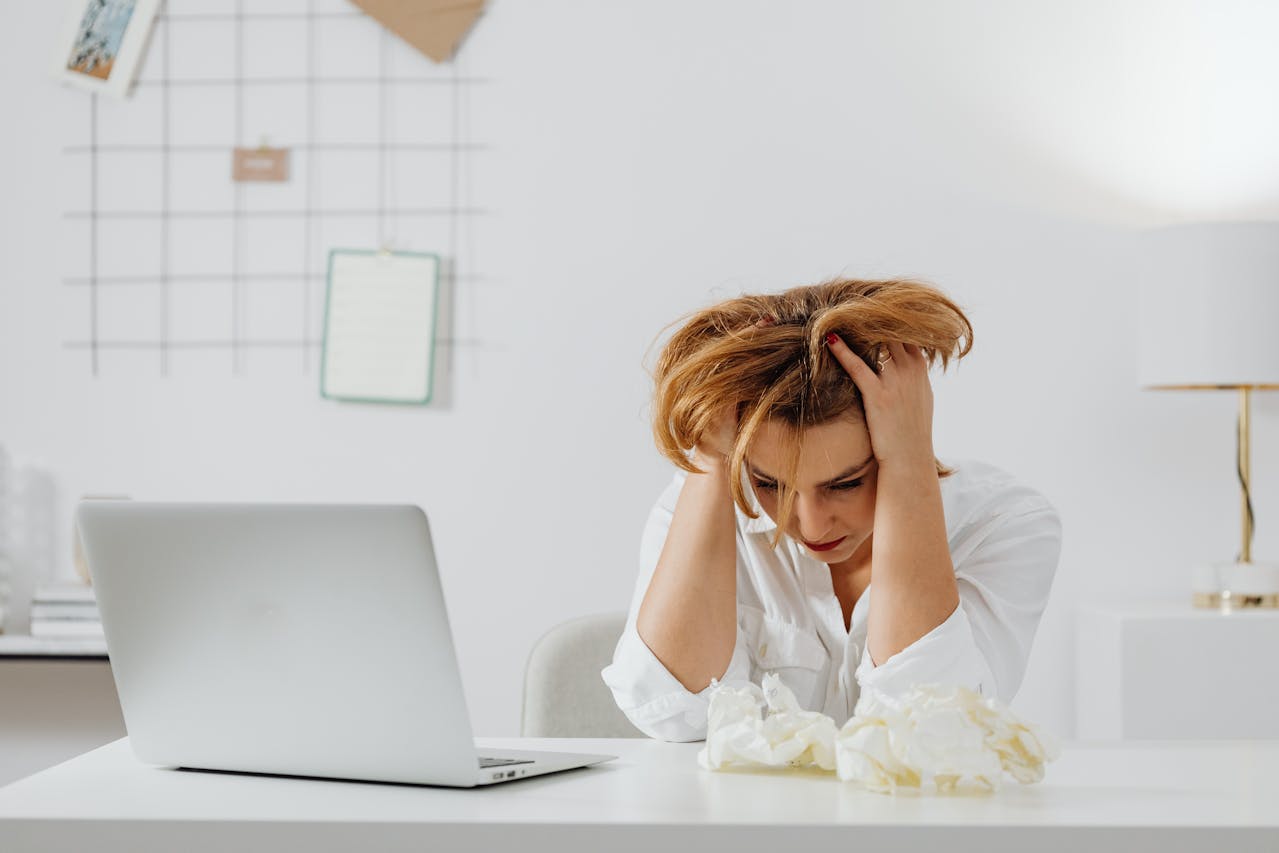 a woman looking distressed sitting next to a laptop to demonstrate the negative effects of dark patterns and mental health